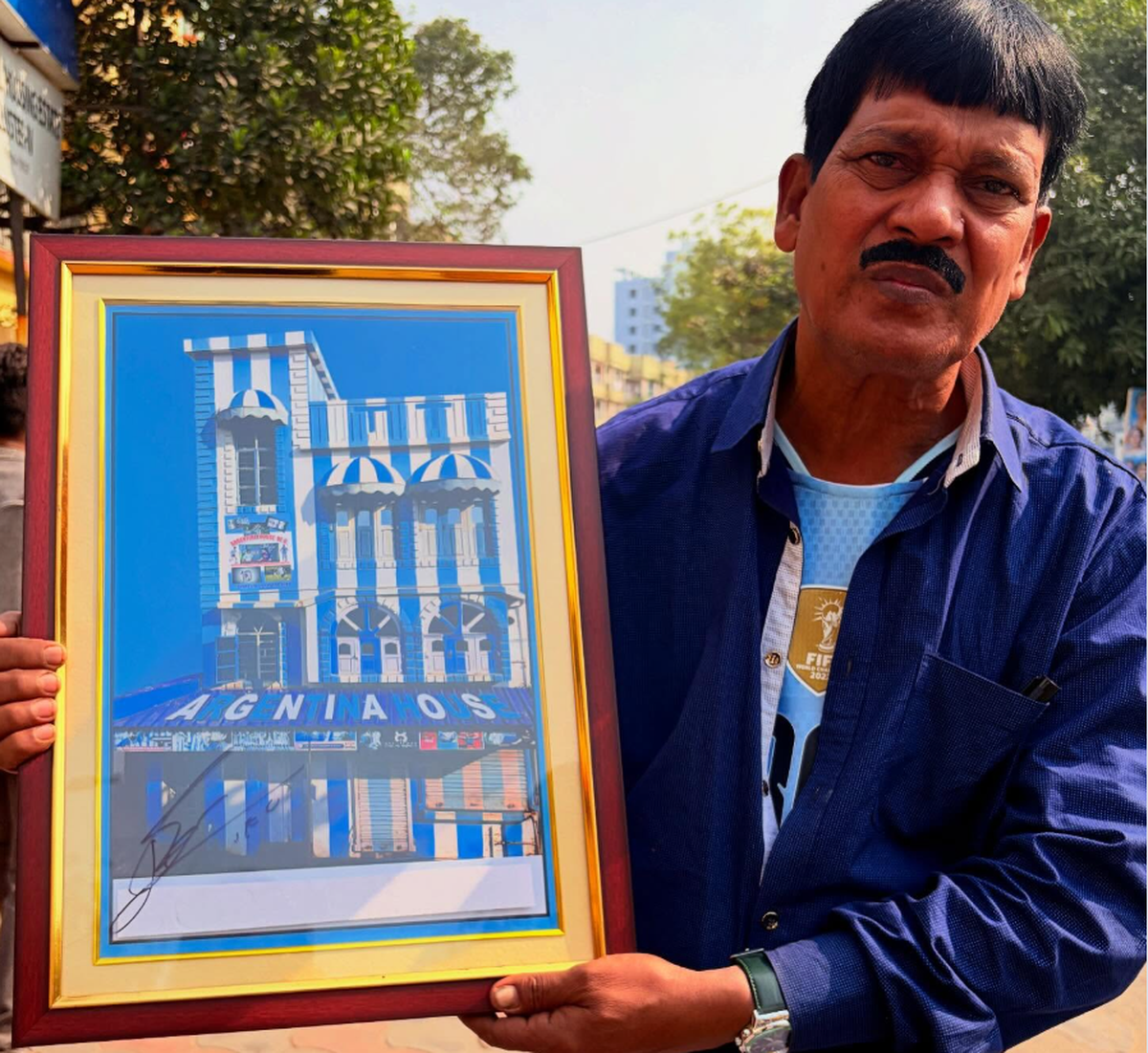 Shibe da holding a framed phtotograph of his Argentina themed home signed by Lionel Messi